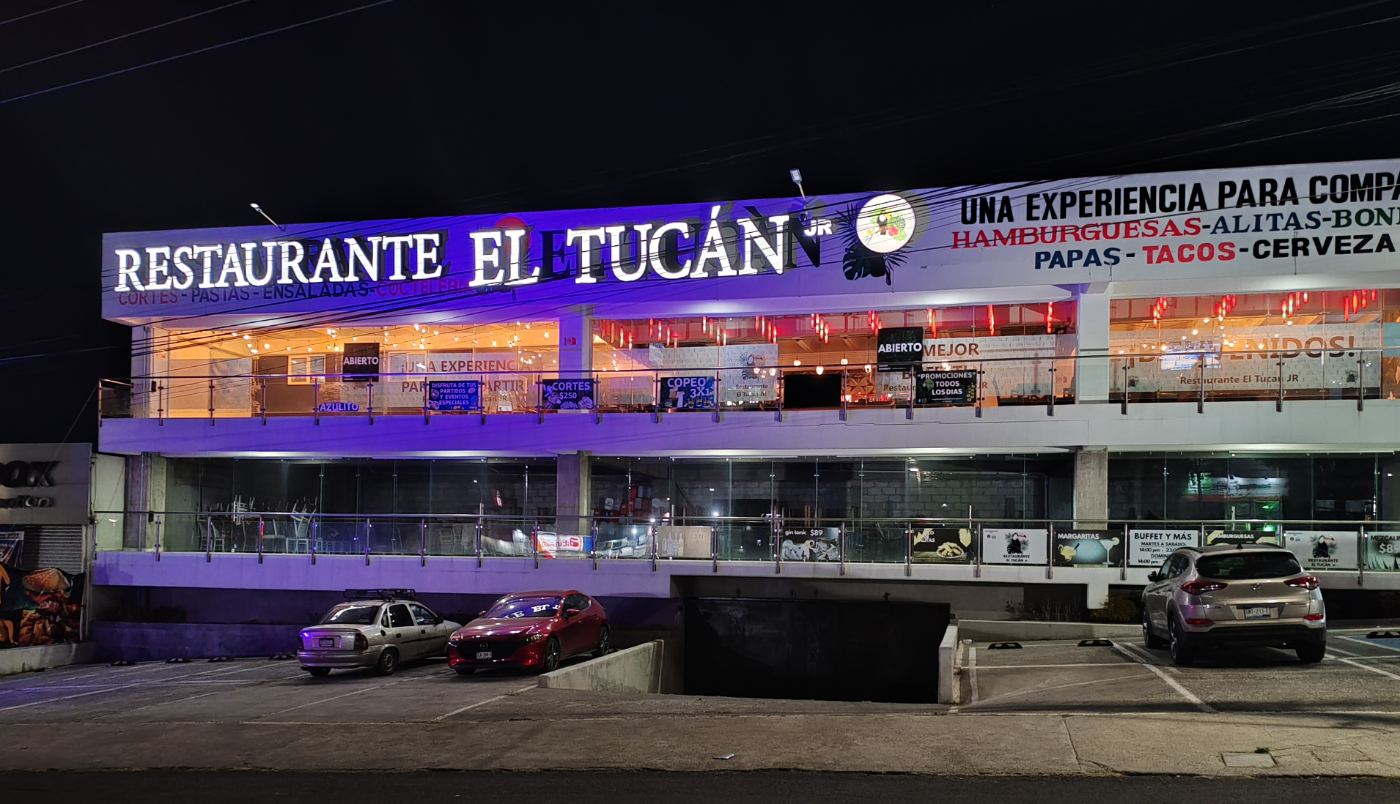 La fachada de El Tucán JR de noche, con el rótulo iluminado sobre Av. del Parque.