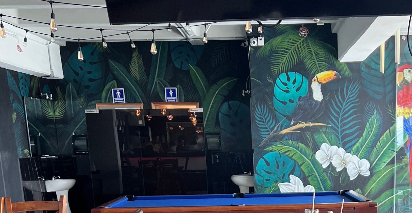 El mural de selva del salón, pintado a mano, con un tucán y un guacamayo entre hojas de monstera y orquídeas.